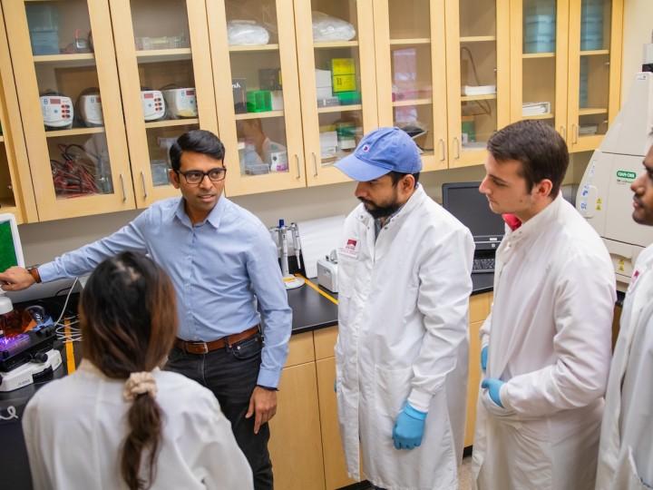 A faculty member teaches students wearing lab coats